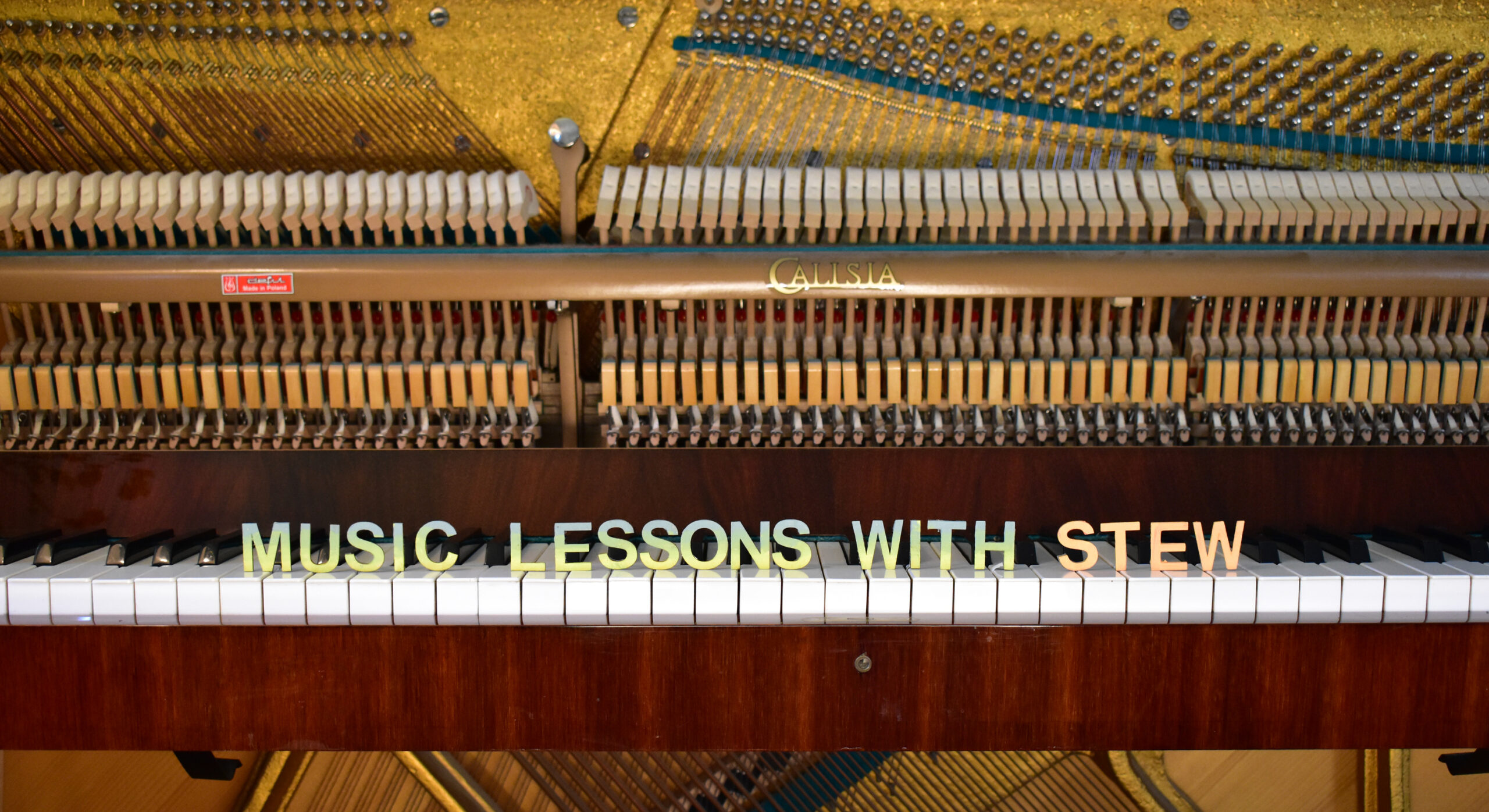 An image of a piano keyboard with painted wooden letters spelling out Music Lessons with Stew on the keys.