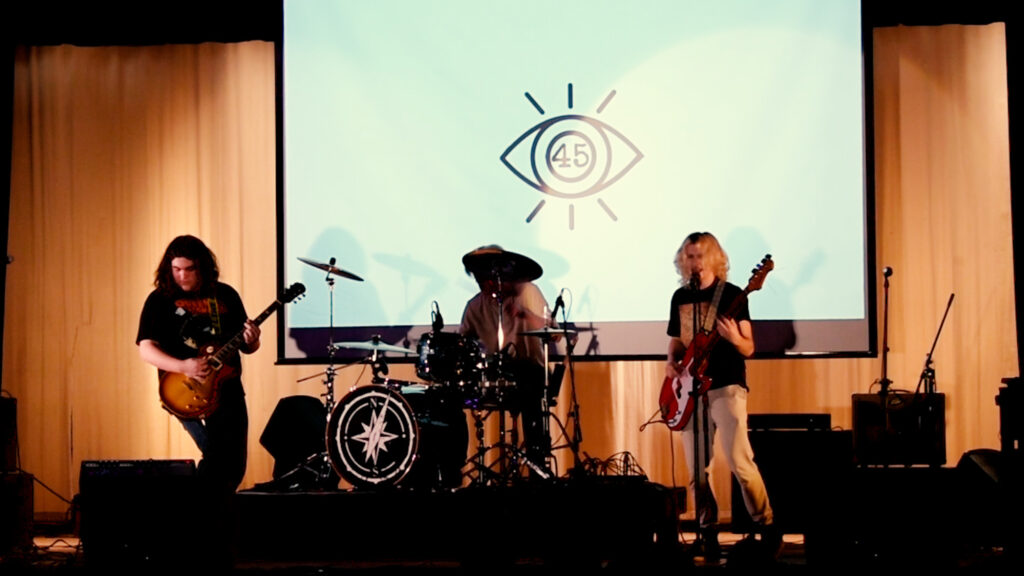 Image of a group pf high school musicians playing on a stage in a high school auditorium